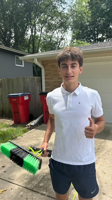 Noah Green, owner of CU Window Wash, giving a thumbs up and holding his window-cleaning brush outside a Champaign-Urbana home